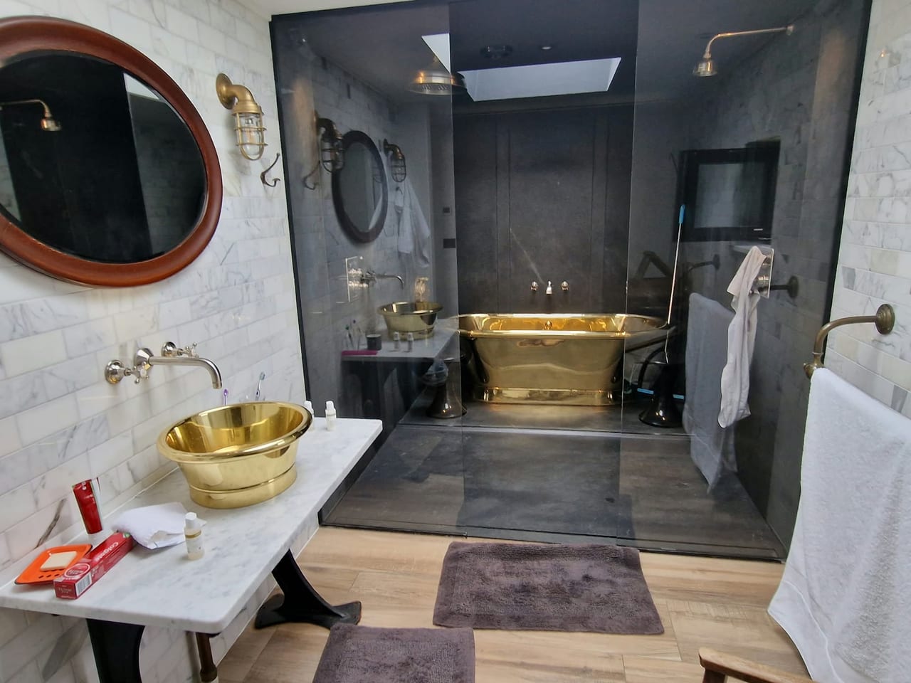 Bathroom with a gold-coloured freestanding bath, gold basin and dark tiled walls.