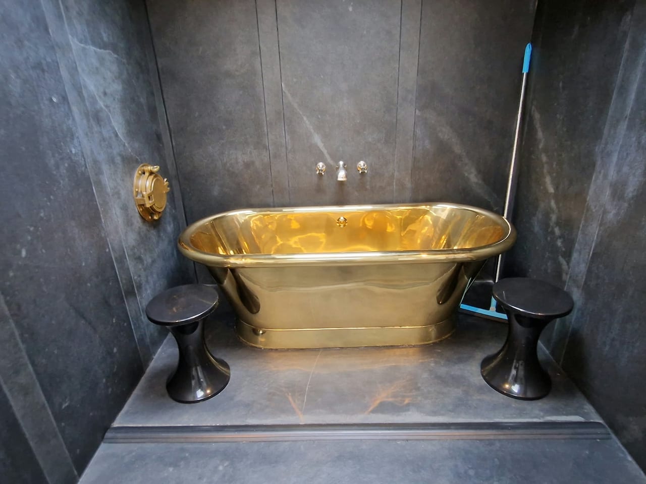 Gold-coloured freestanding bath in a dark tiled alcove.