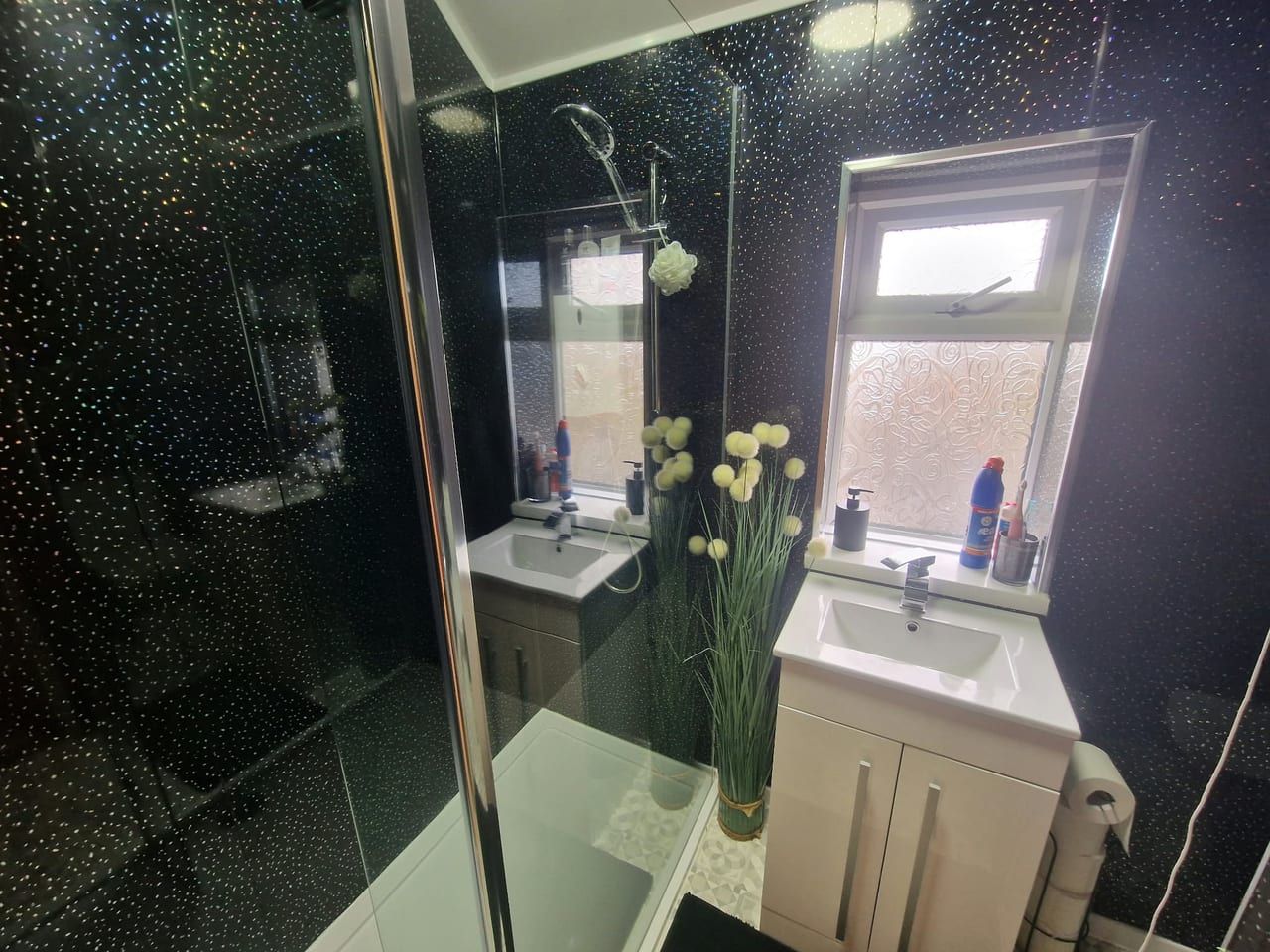 Bathroom with a glass shower enclosure, white basin cabinet and dark mosaic wall tiles.