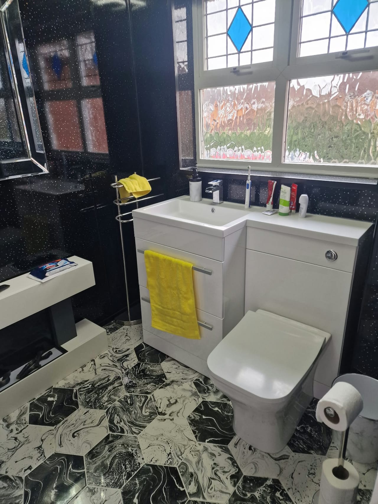 Bathroom with a white bath and toilet, dark walls and patterned floor tiles.