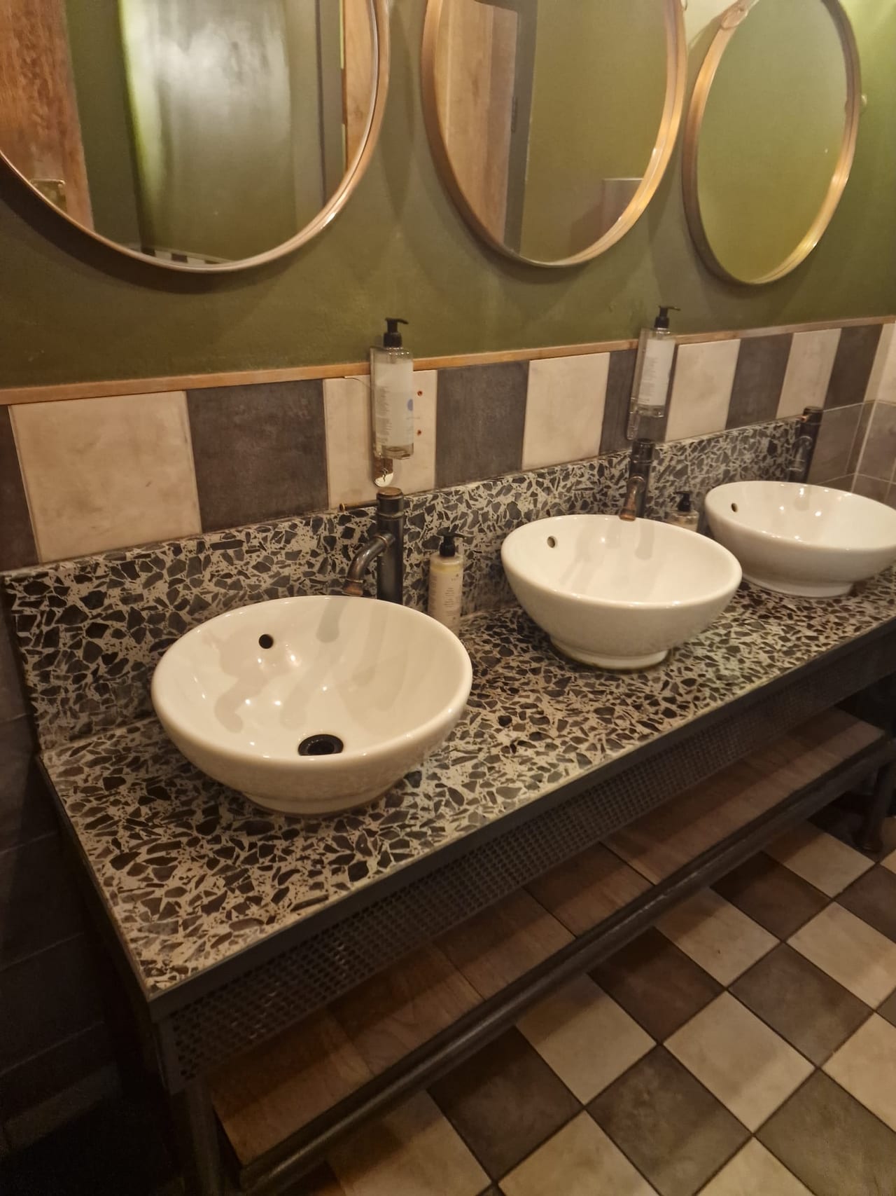 Three white countertop basins beneath round mirrors, with patterned wall and floor tiles.