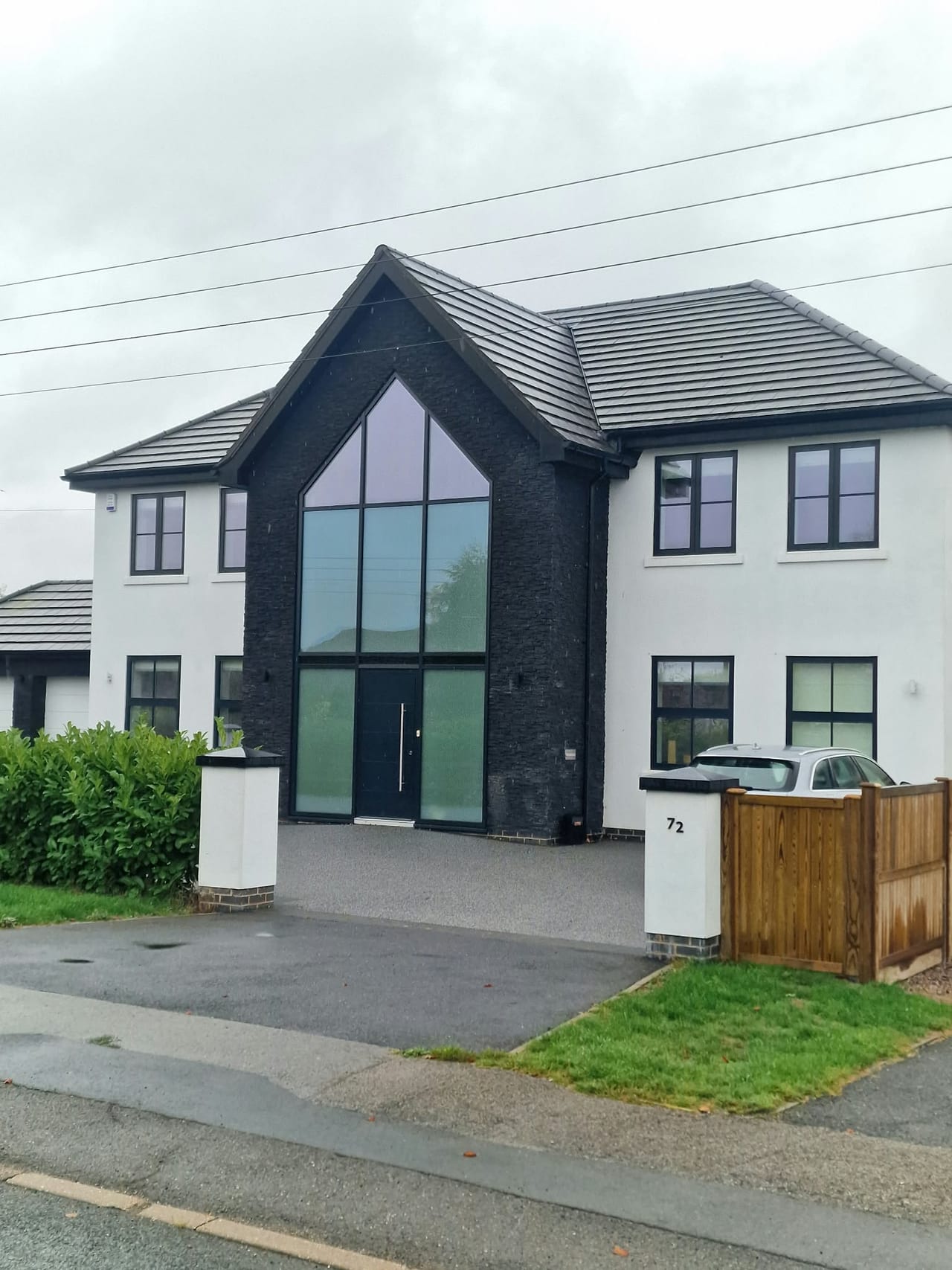 White house frontage with a tall black-framed glazed entrance and pitched roof.