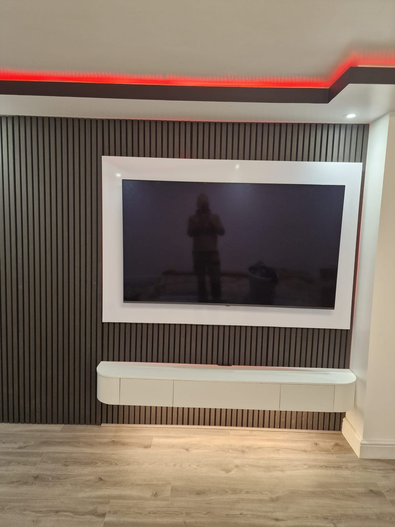 Television within a dark vertically panelled feature wall, with a white radiator below.