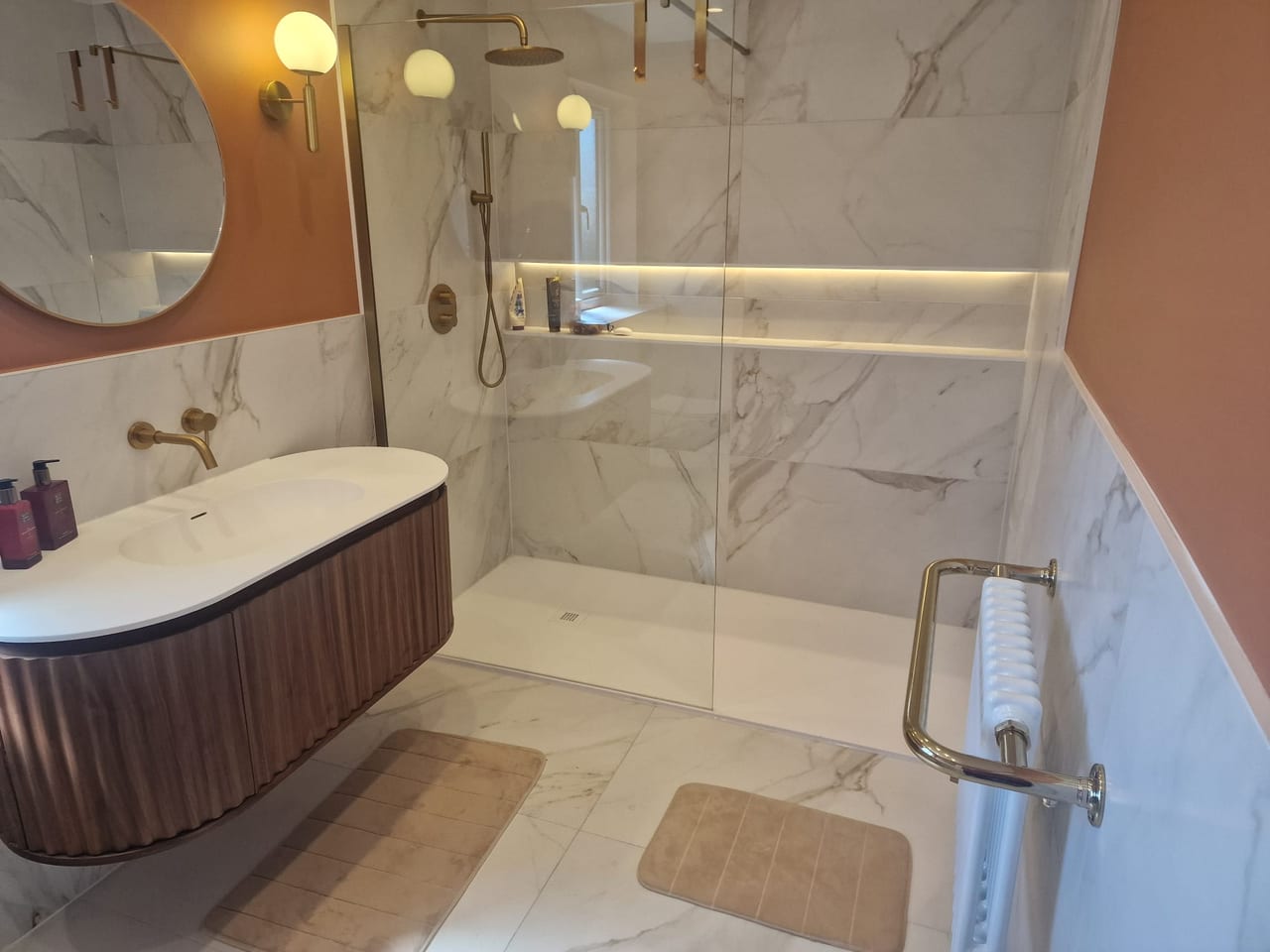 Bathroom with a glass walk-in shower, curved basin cabinet and pale marble-effect tiles.