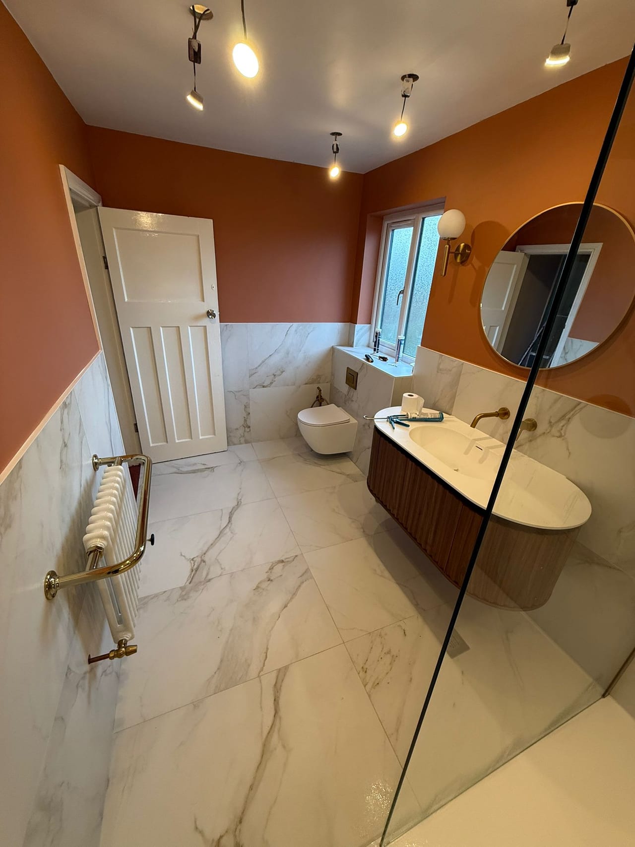 Bathroom with a glass shower screen, curved basin cabinet and terracotta-coloured upper walls.