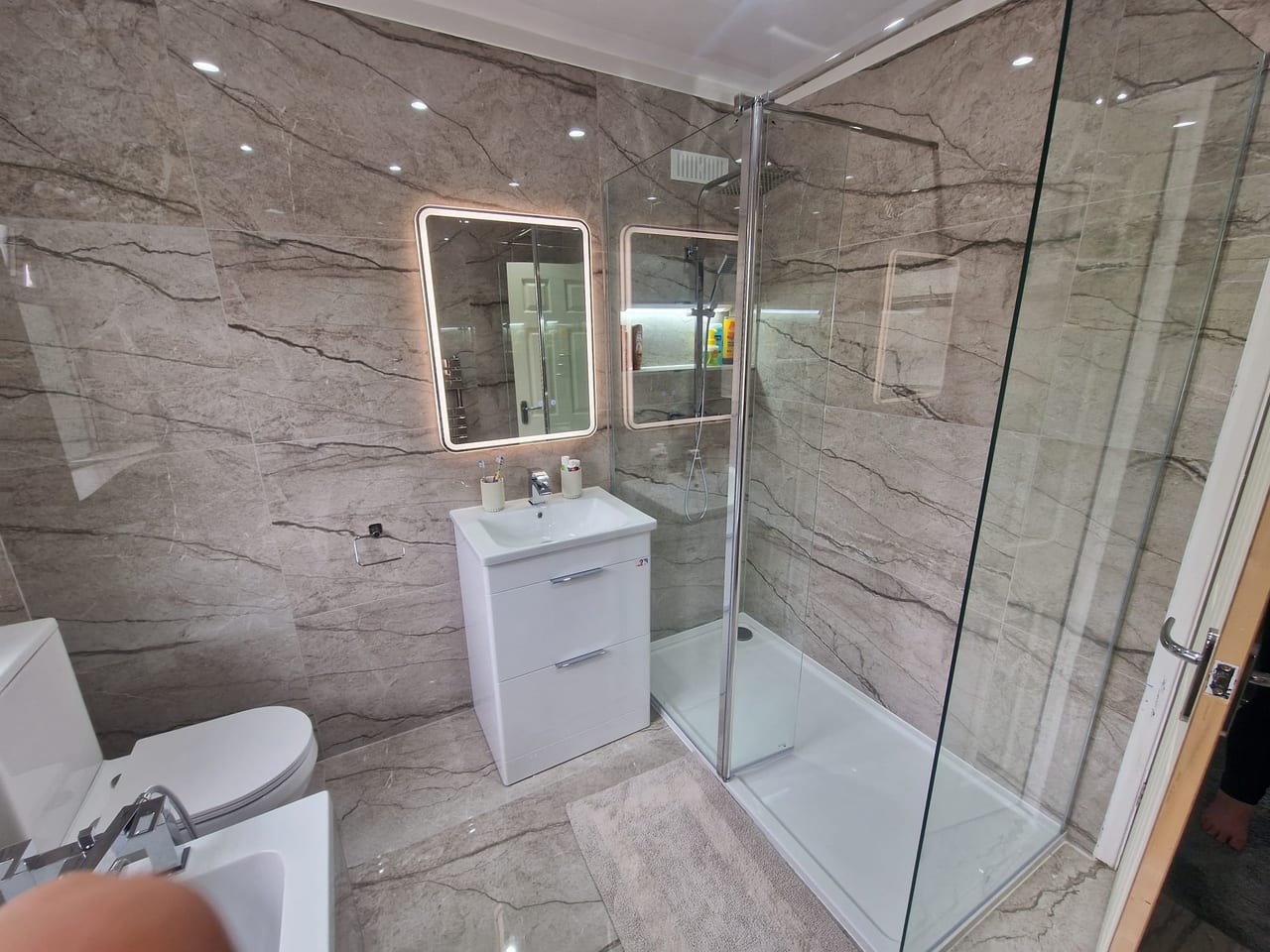 Bathroom with a glass shower enclosure, white basin cabinet and grey marble-effect wall tiles.