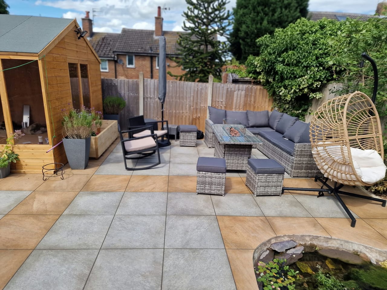 Paved garden patio with outdoor sofas, a hanging chair, timber fencing and planting.