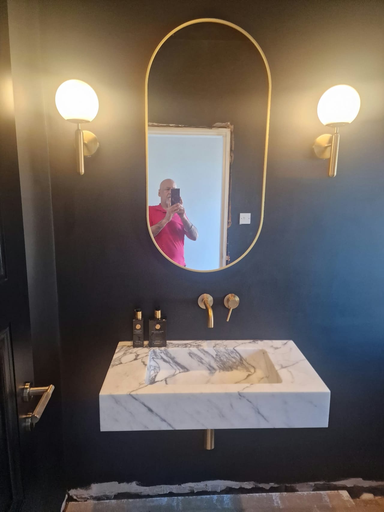 Marble-effect basin beneath an oval mirror and two wall lights against dark walls.
