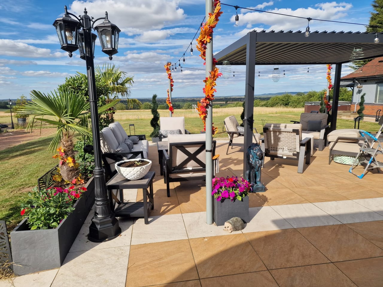 Paved outdoor seating area with a pergola, decorative lamp post and planted pots.