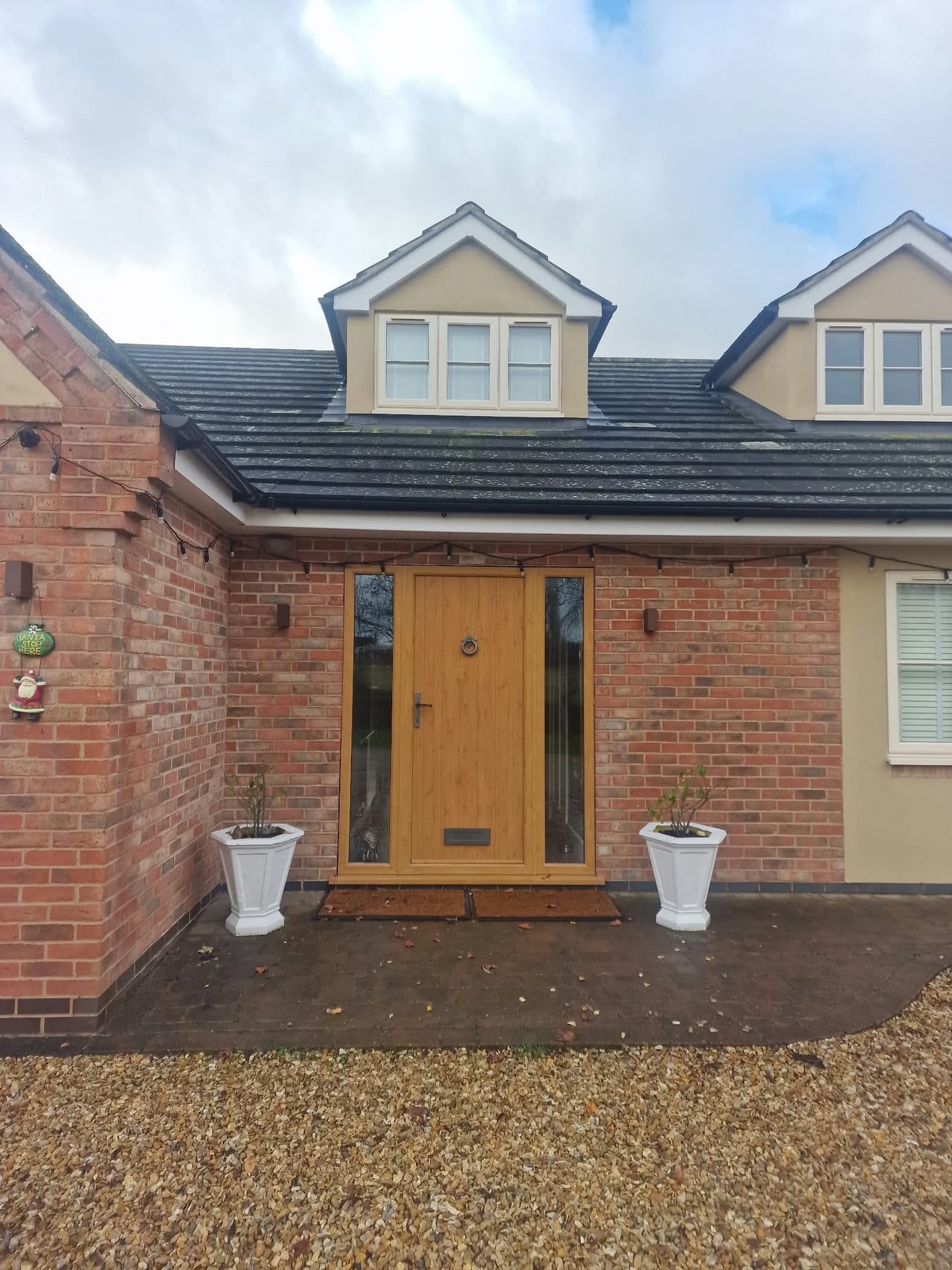 Brick house entrance with timber double doors, two dormer windows and a gravel driveway.