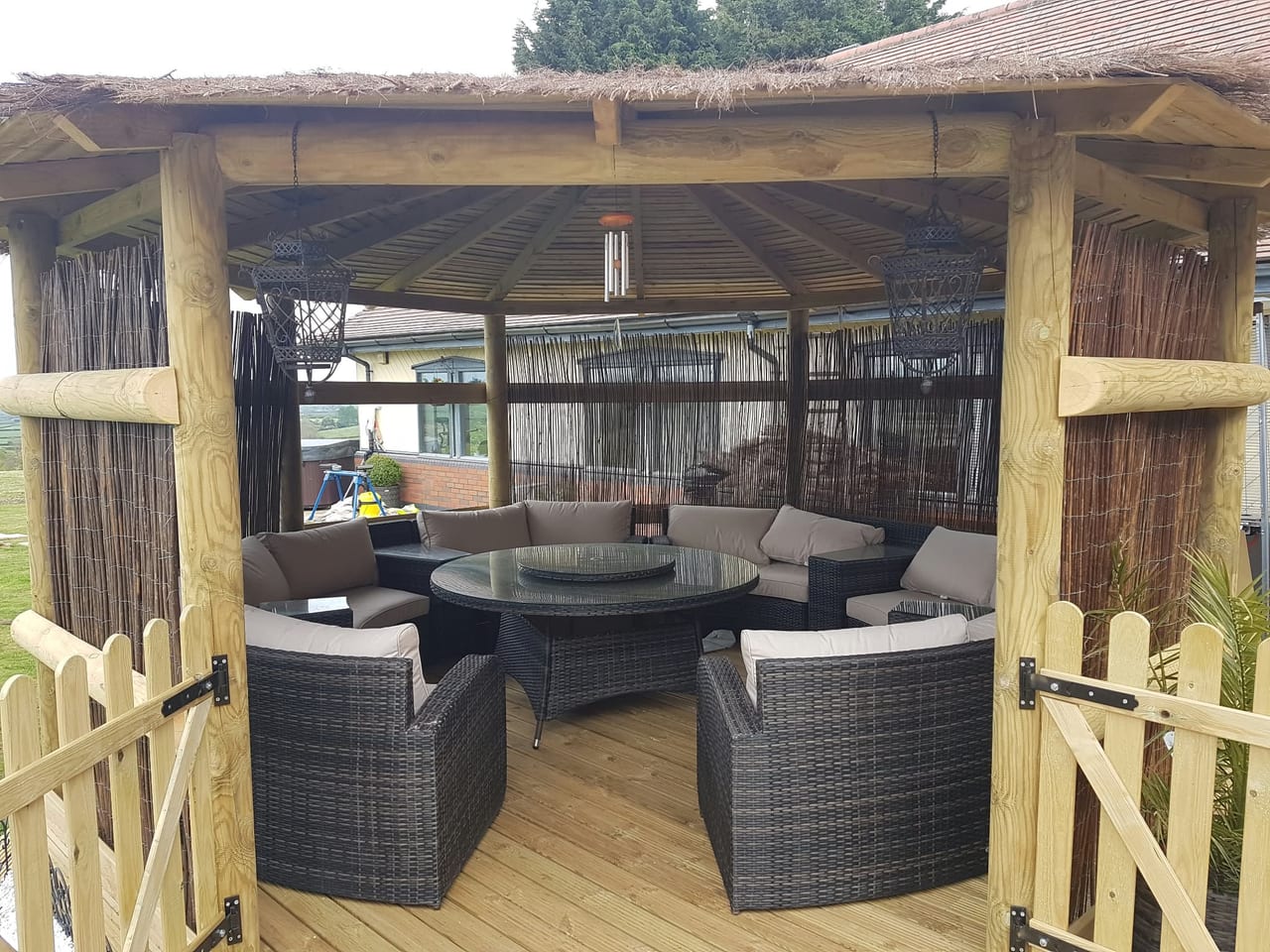 Timber garden gazebo containing woven outdoor chairs and a table.