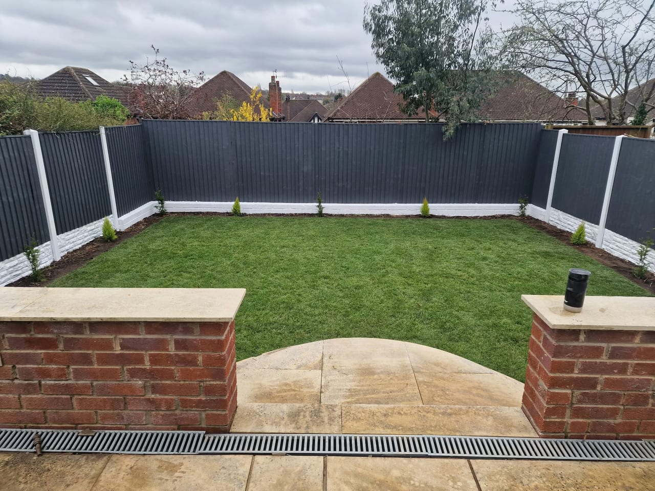 Enclosed lawn with dark fence panels, brick retaining walls and a paved entrance.