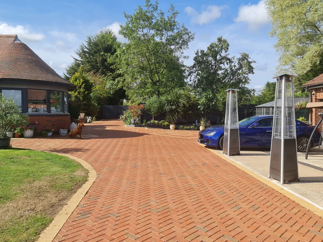 Curving red block-paved driveway beside a brick house and landscaped garden.