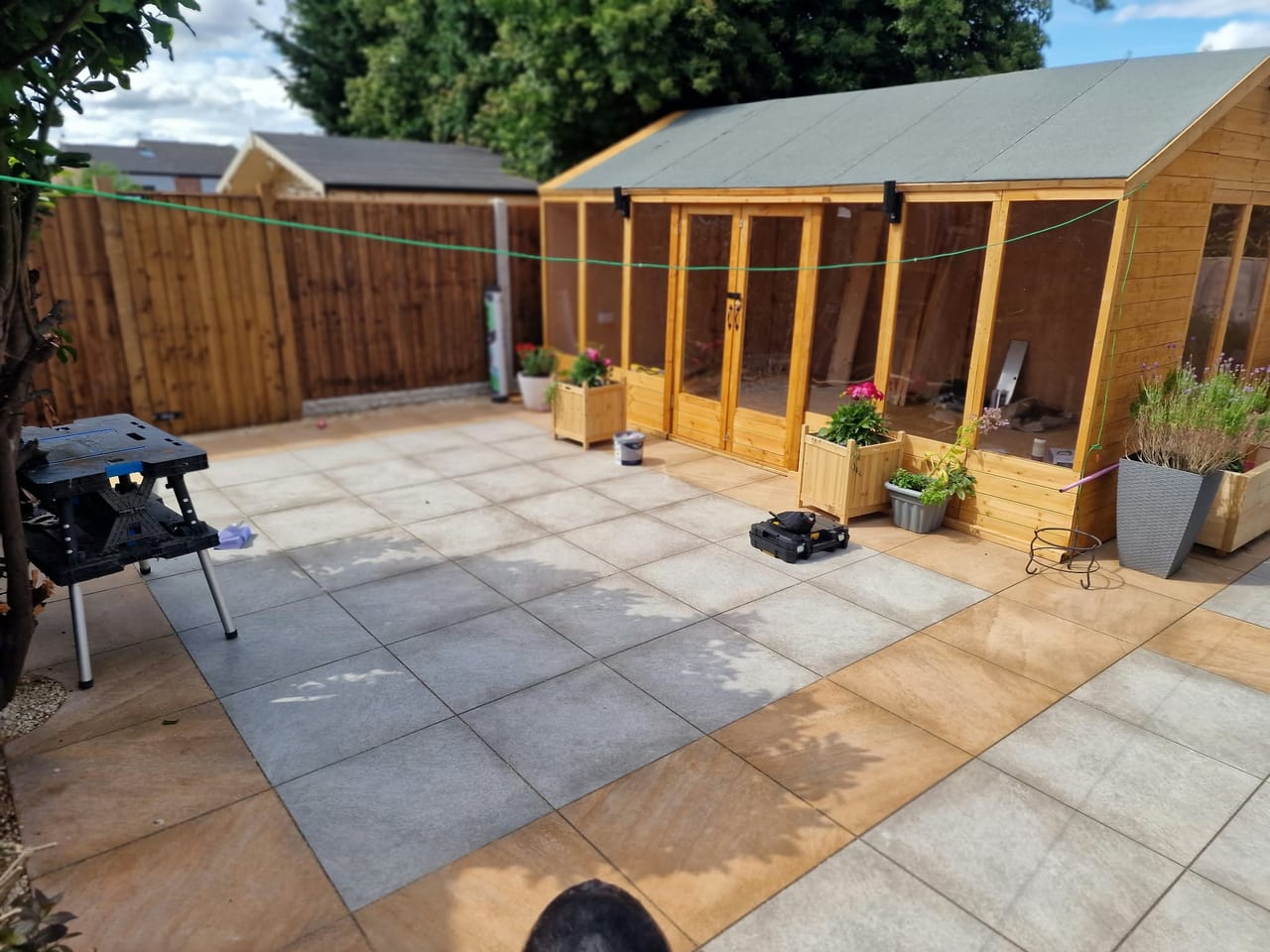 Paved garden patio beside a timber garden building, with fencing and planted pots.