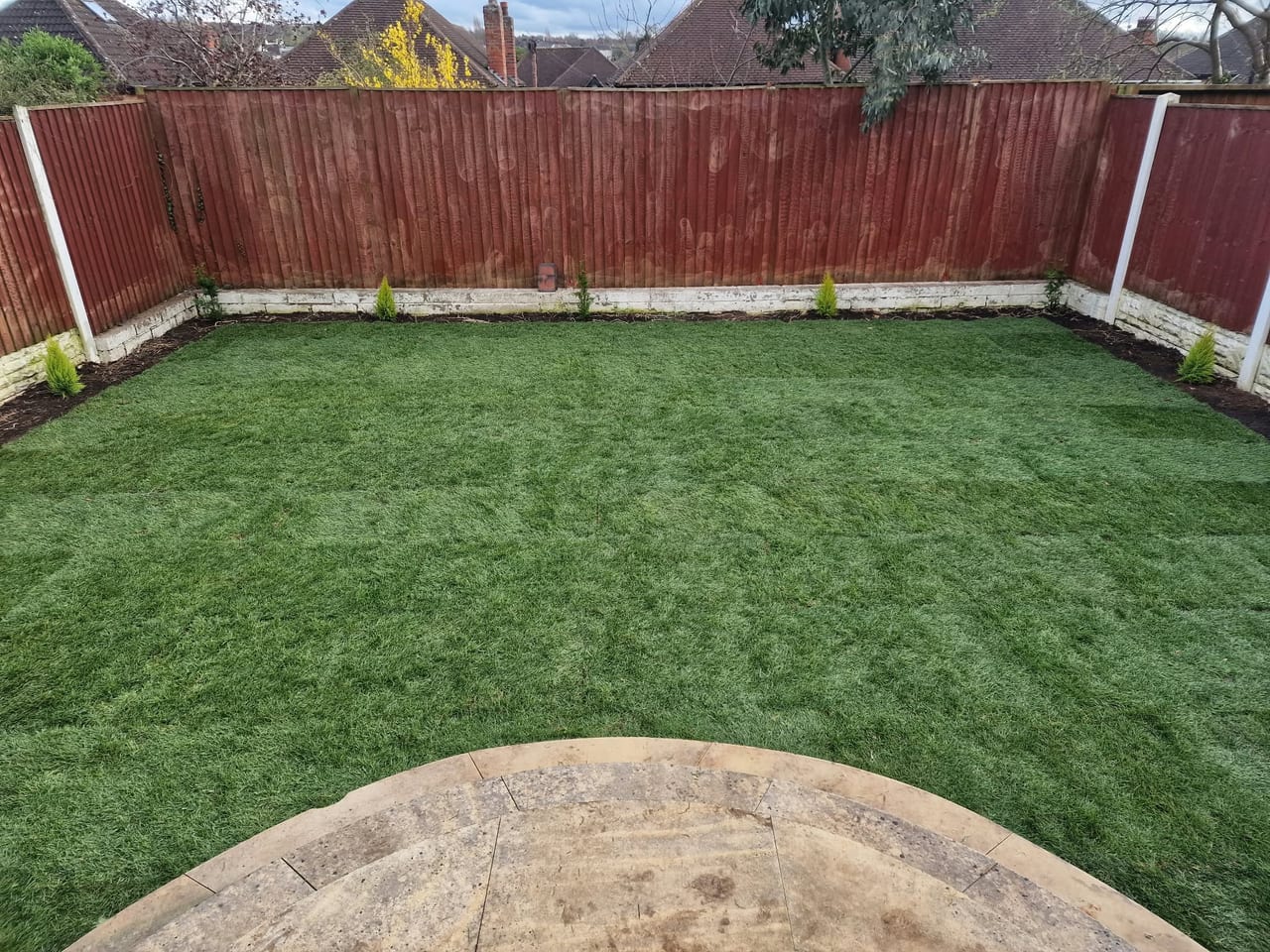 Garden lawn enclosed by timber fencing with a curved paved area in the foreground.