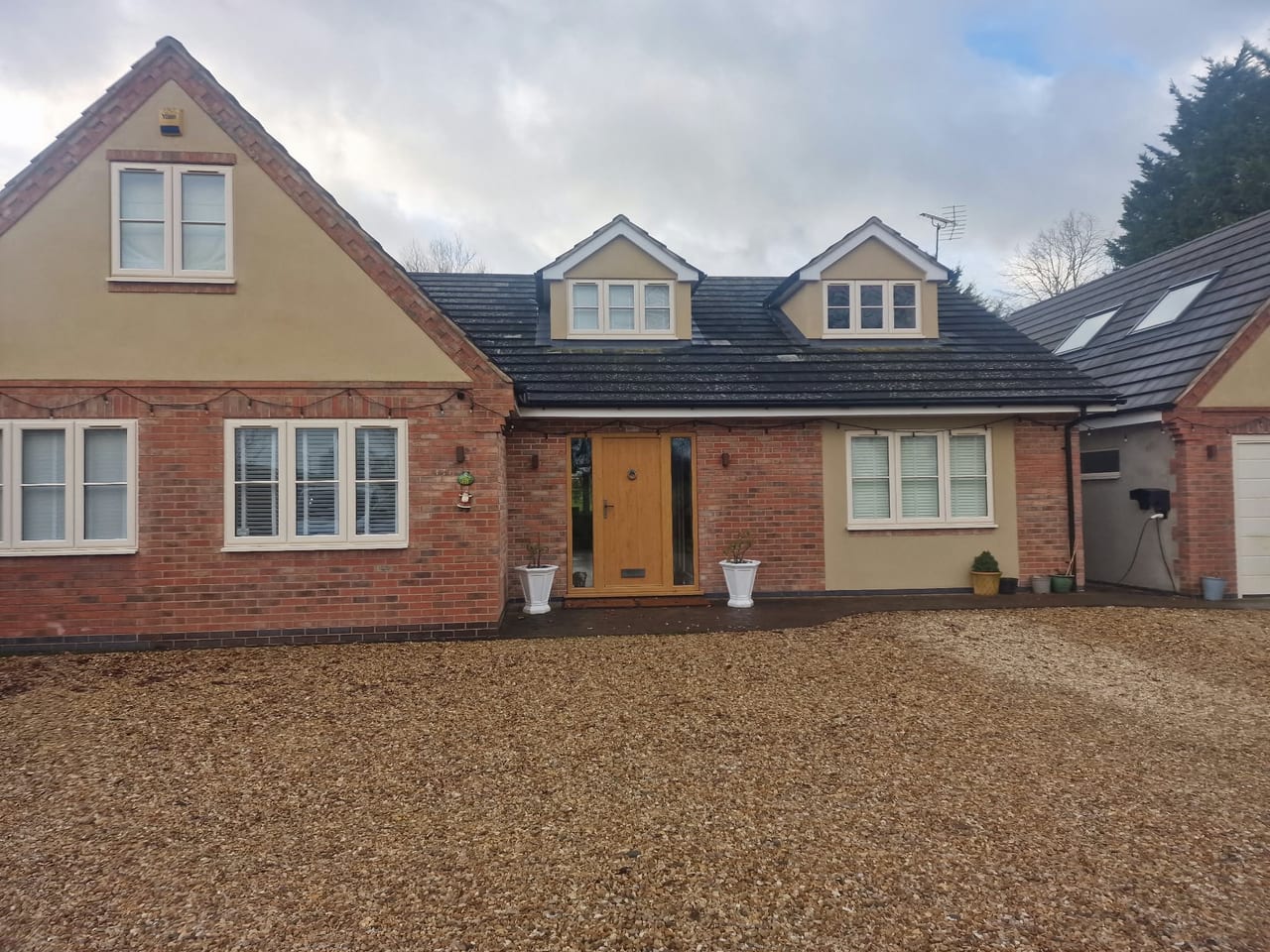 Brick house frontage with a pitched roof, dormer windows and a wide gravel driveway.