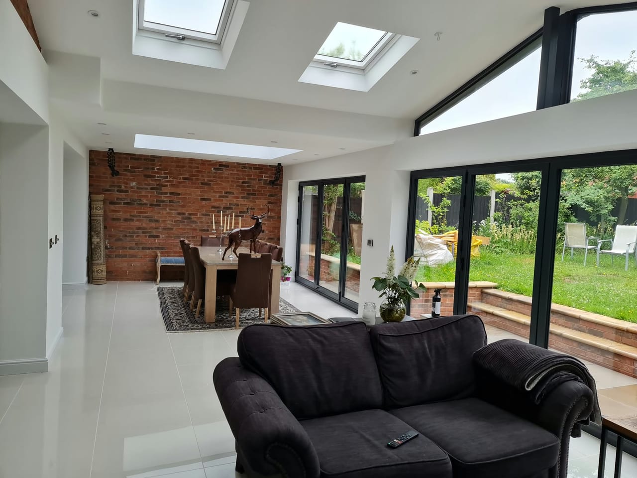 Bright living and dining space with rooflights, black-framed glass doors and an exposed brick wall.